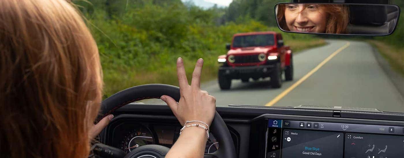 Woman driving a 2025 Jeep Wrangler past a red Jeep Gladiator.