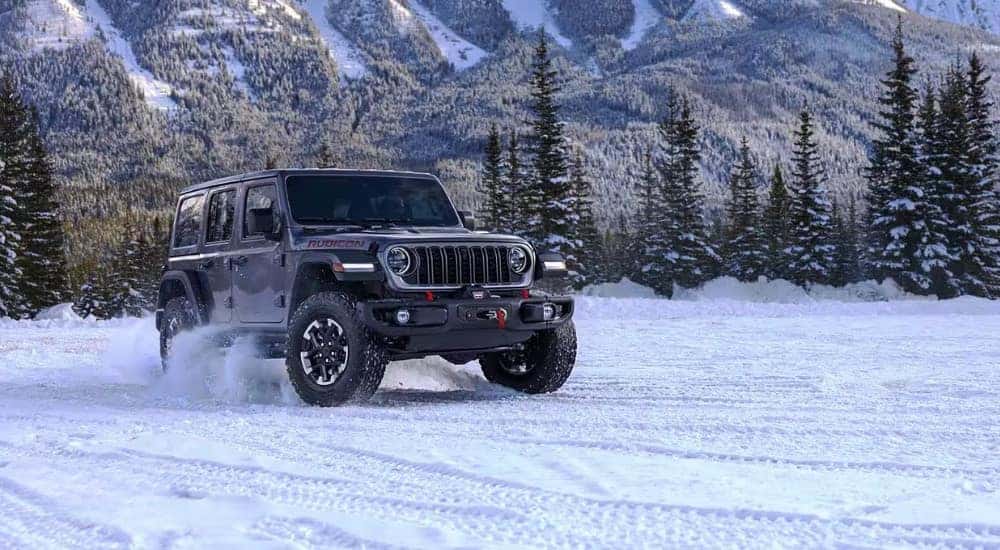 A grey 2025 Jeep Wrangler for sale driving through snow.