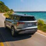 A silver 2026 Chevy Equinox for sale driving near a lake.