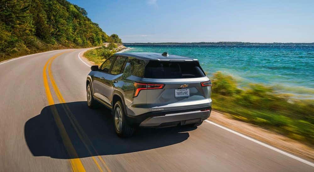 A silver 2026 Chevy Equinox for sale driving near a lake.