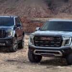 A black 2025 GMC Yukon Denali and a gray 2025 GMC Yukon AT4 parked off-road
