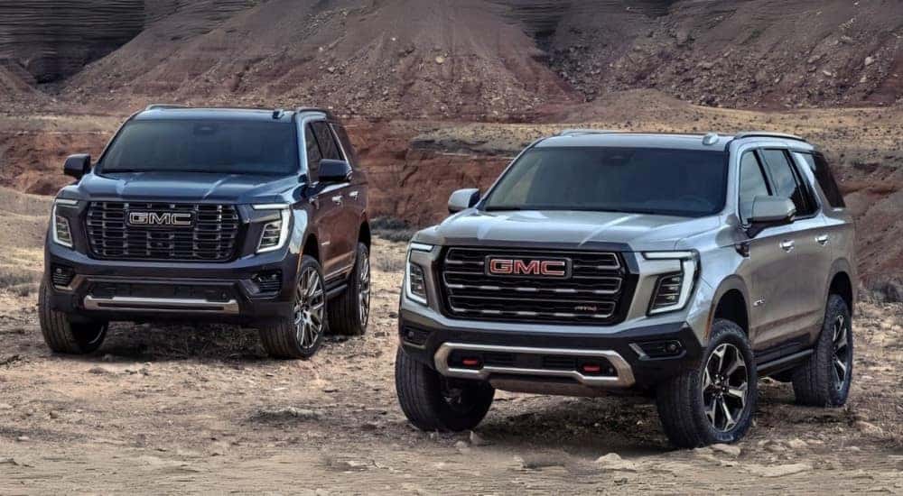 A black 2025 GMC Yukon Denali and a gray 2025 GMC Yukon AT4 parked off-road