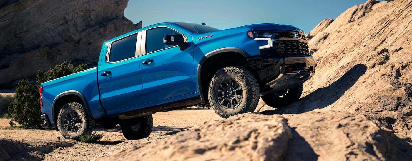 A blue 2024 Chevy Silverado 1500 ZR2 driving up a rocky cliff.