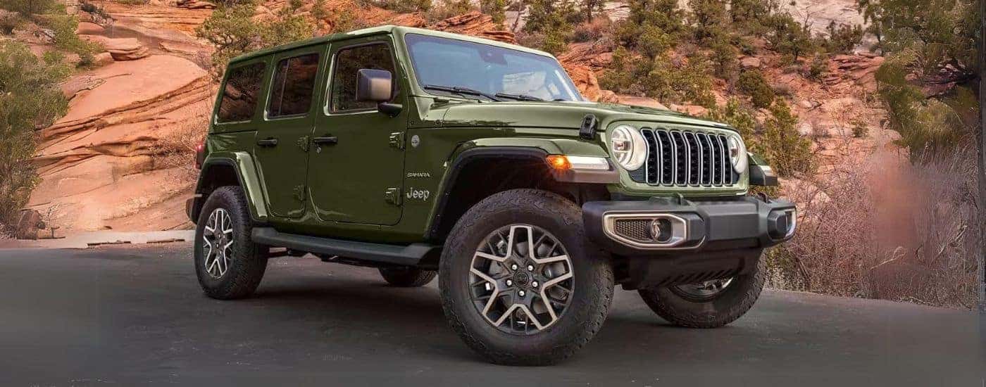 A green 2024 Jeep Wrangler Sahara Unlimited parked in front of rocks.