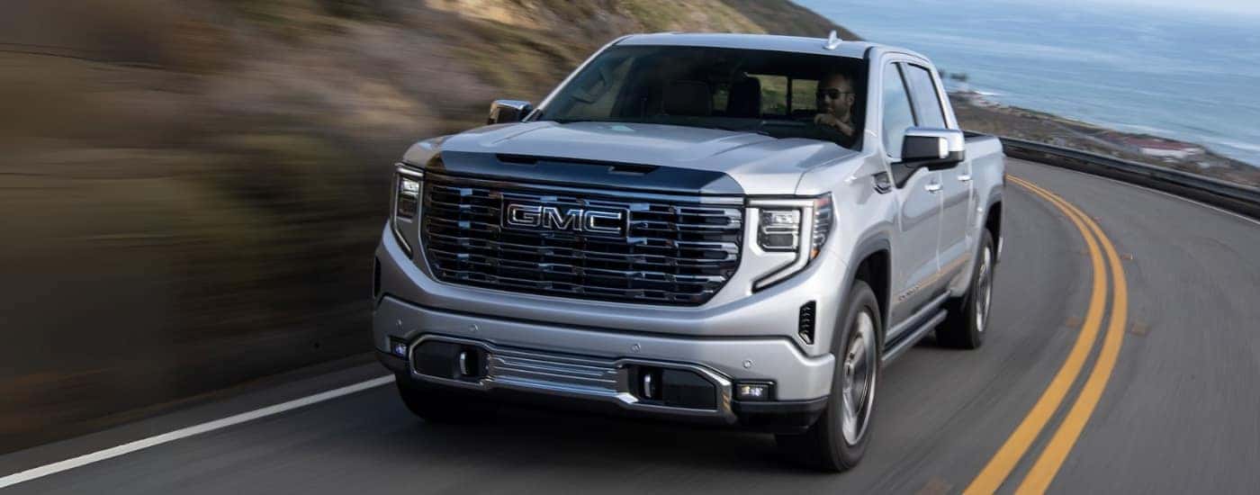 A silver 2024 GMC Sierra 1500 is shown driving on a highway after viewing trucks for sale near Alamosa.