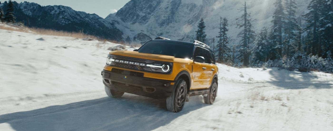A popular vehicle for Alamosa auto sales, a yellow 2022 Ford Bronco Sport Badlands, is shown driving on a snowy trail in the mountains.