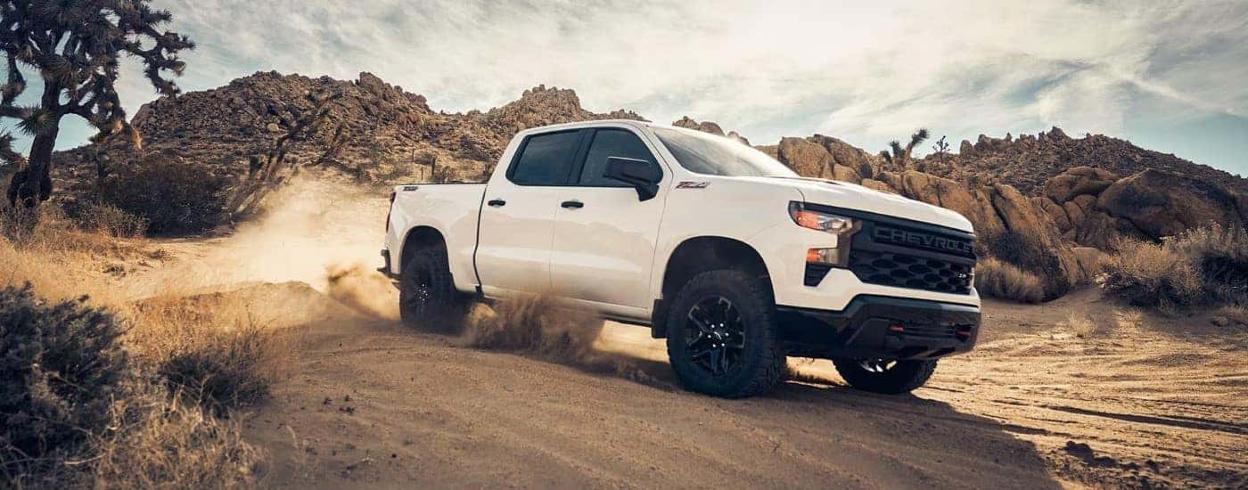 A white 2024 Chevy Silverado 1500 Z71 Trail Boss is shown from the front at an angle after leaving a dealer that has a Chevy Silverado for sale.