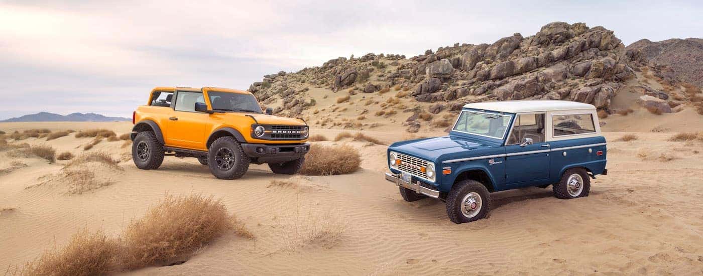 A blue 1966 Ford Bronco and an orange 2021 Bronco are shown parked next to each other.