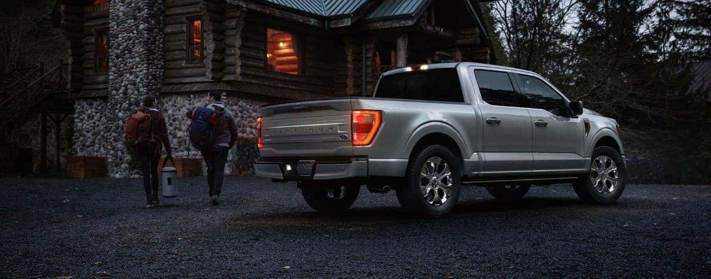 A silver 2021 Ford F-150 Platinum is shown from the rear parked outside of a cabin at night.