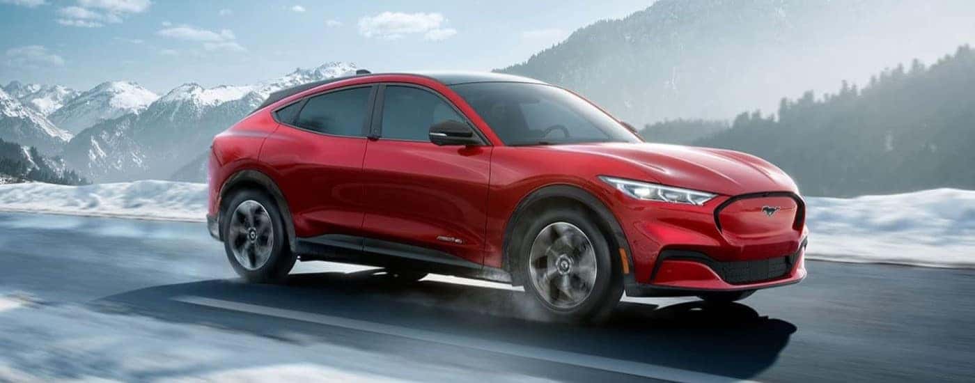 A red 2022 Ford Mustang Mach-E is shown driving on a snowy road after learning about EV performance in cold weather.