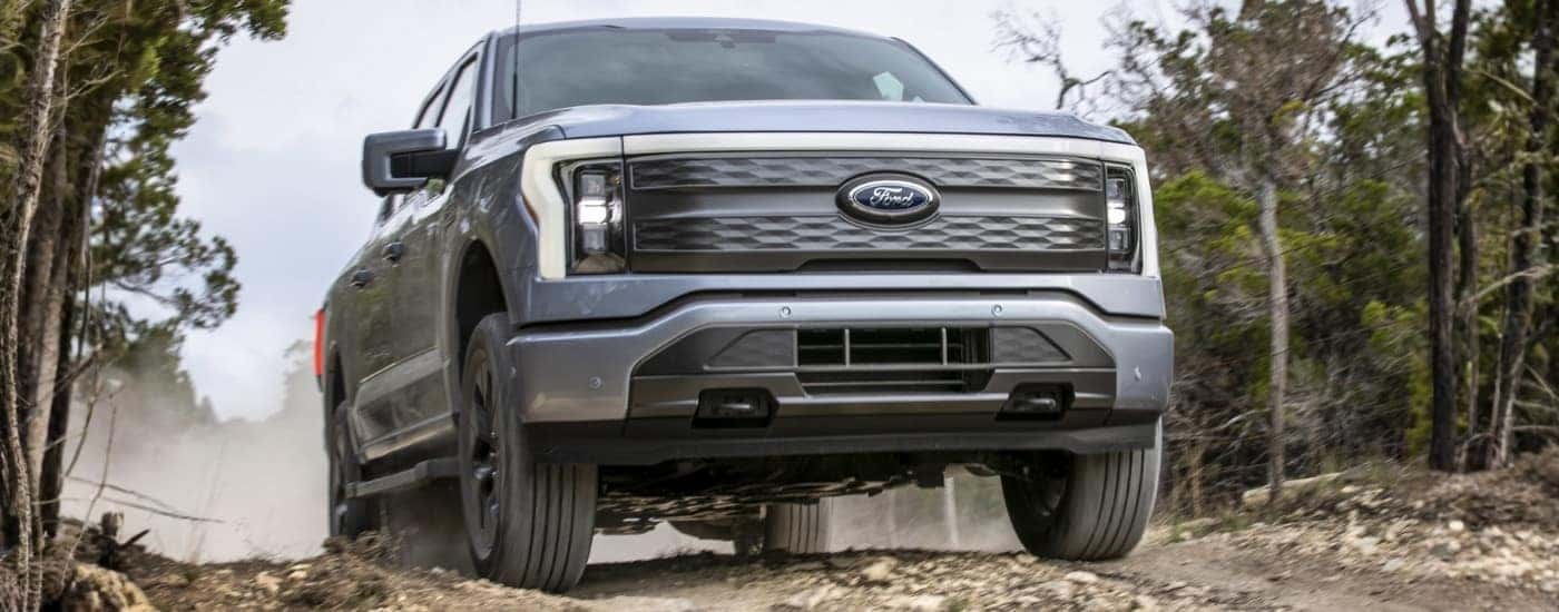 A silver 2022 Ford F-150 Lightning is shown from the front while driving off-road.