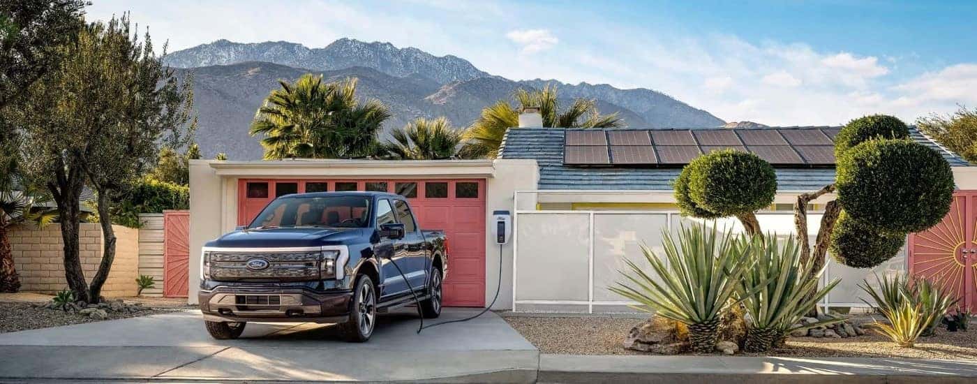 A black 2023 Ford F-150 Lightning is shown charging at a house.