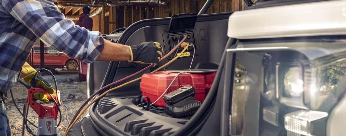A close up shows someone using the power outlets under the hood of a white 2023 Ford F-150 Lightning.