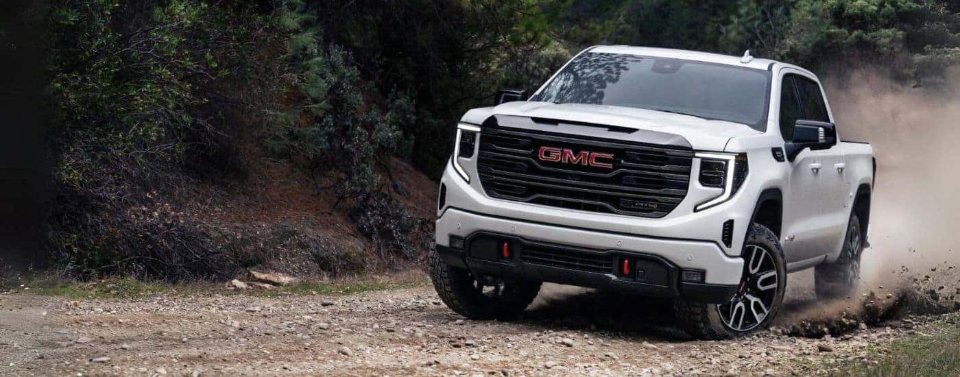 A white 2023 GMC Sierra 1500 AT4 is shown from the front driving on a dirt road.