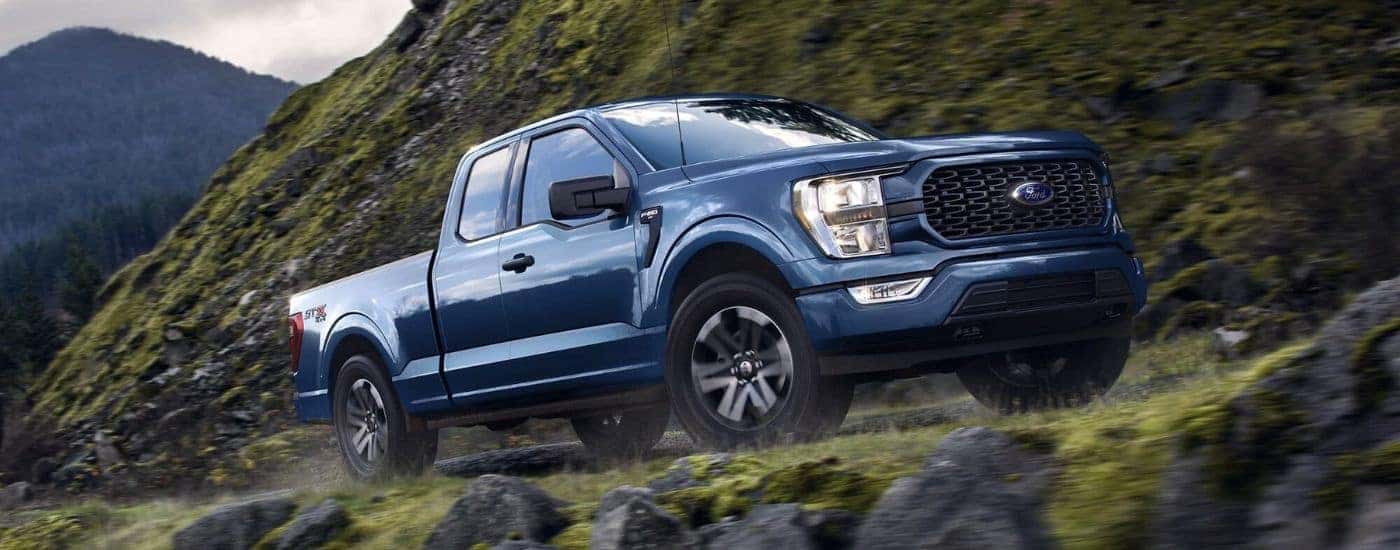 A blue 2023 Ford F-150 STX is shown from the side while off-road after leaving a truck dealership.